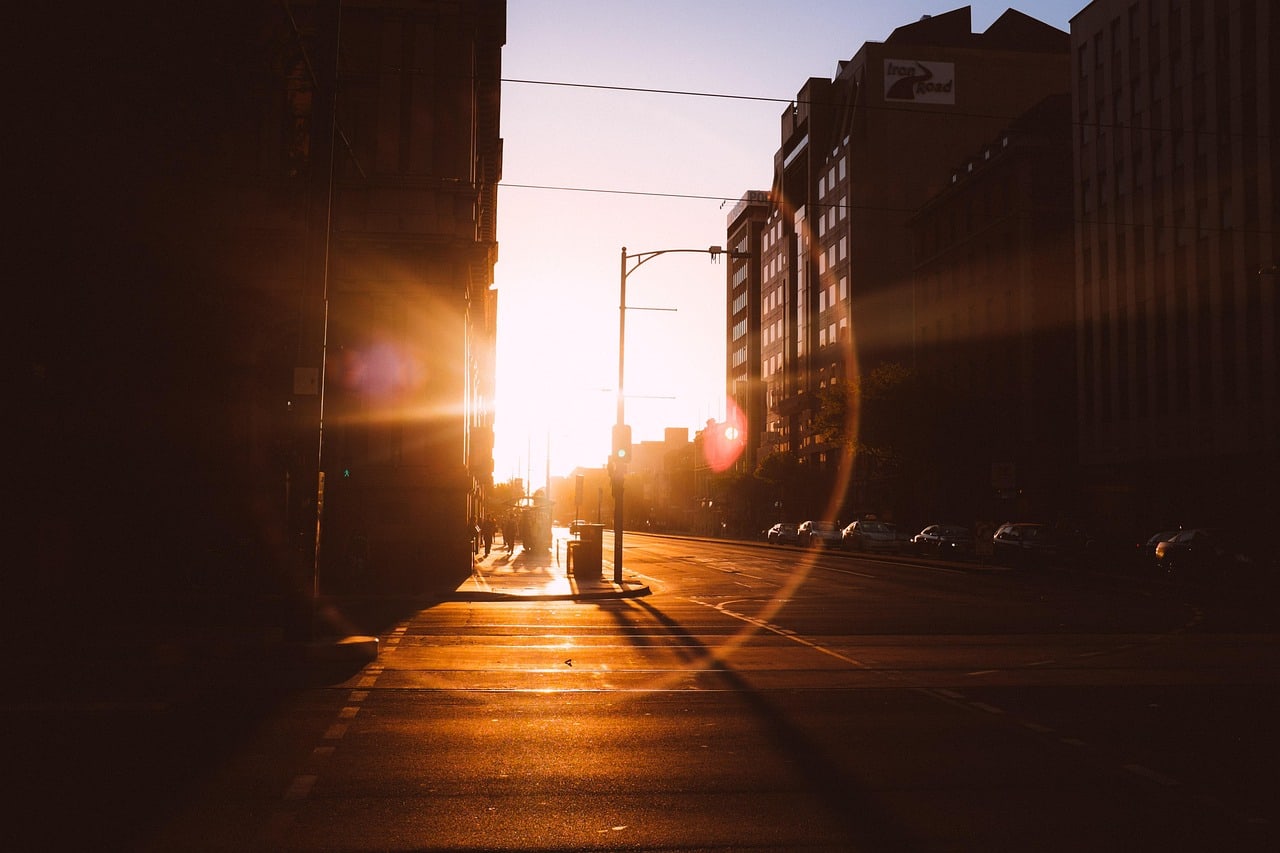 Low sun shining between city buildings and casting long shadows across a street