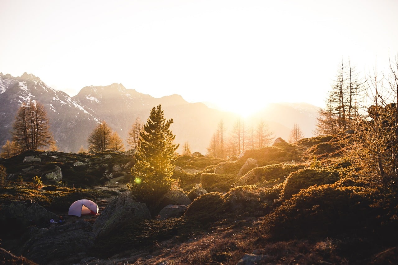 Tent pitched in a sunny mountain campsite with low sunlight over the ridge