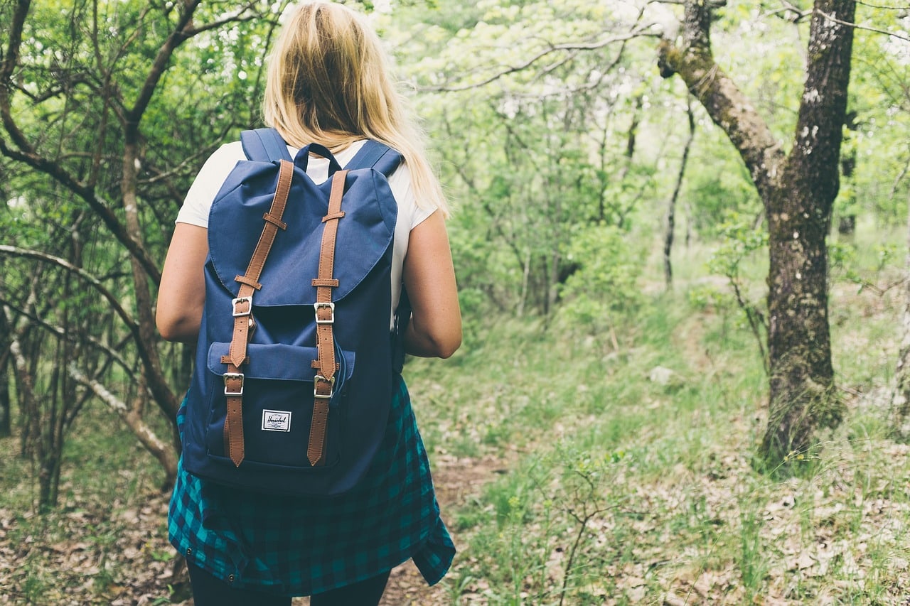 Hiker with a backpack walking beneath trees on a shaded summer trail