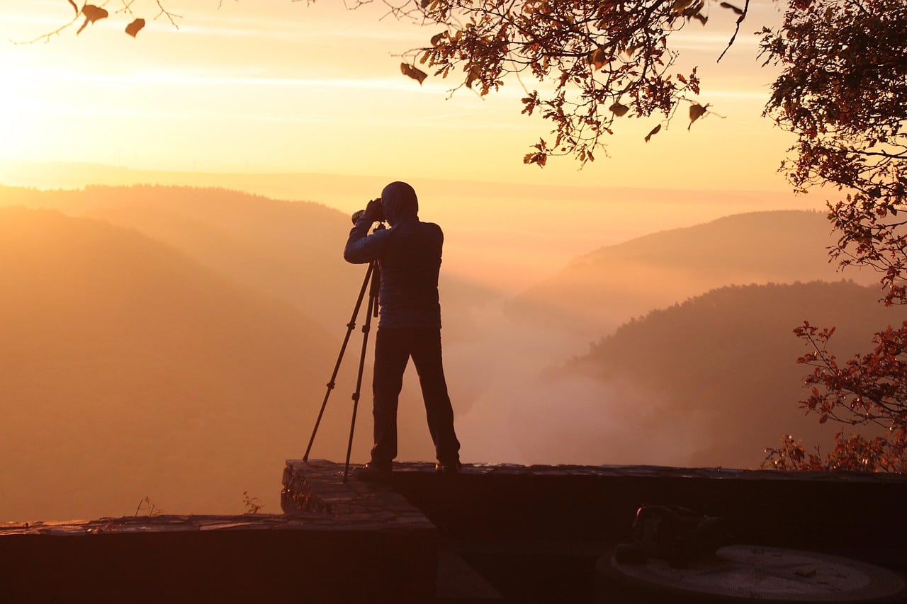 Photographer scouting a mountain landscape at sunrise with a tripod