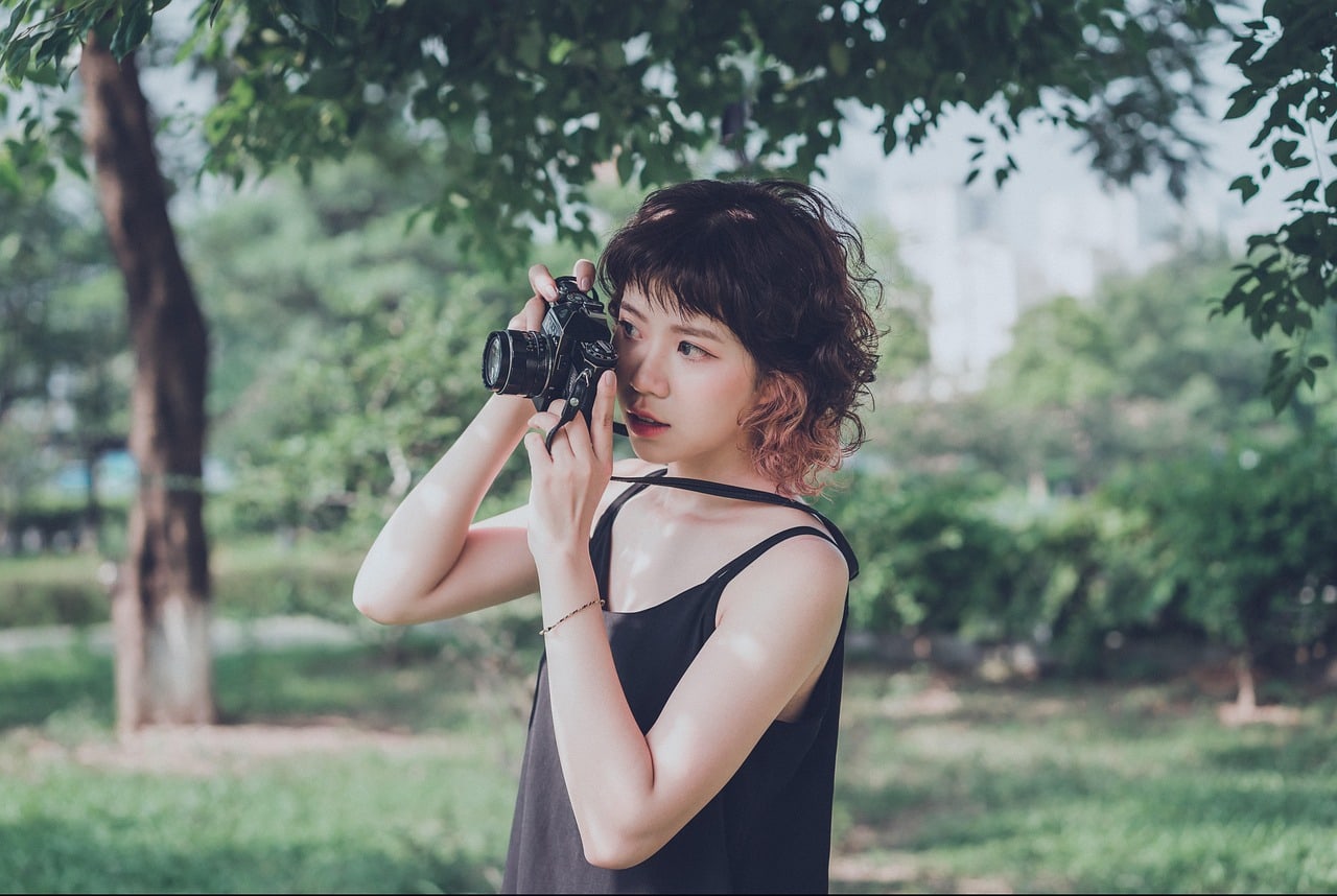 Outdoor photographer holding a camera among green leaves