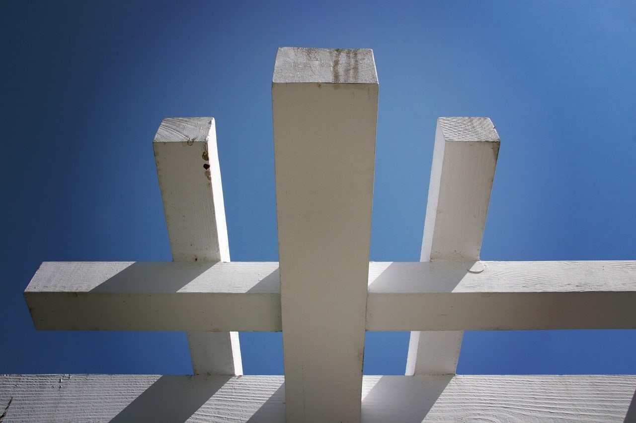 Open white pergola beams casting narrow shadows beneath a clear blue sky